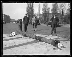Men, including a police officer, look at a broken lamppost