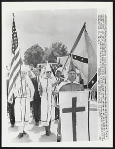 Ku Klux Klansmen framed between American and Confederate flags parade down the city streets of Americus here 8/8. A large crowd gathered at the Sumter County court house to hear Calvin Craig, Grand Dragon of Georgia, and Bobby Shelton, Grand Dragon of the Klan, during the rally.
