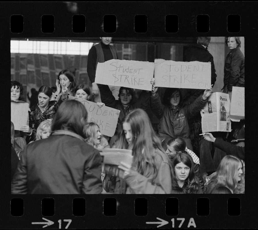 Boston high school students sit on steps at City Hall to display their strike signs during demonstration on City Hall Plaza