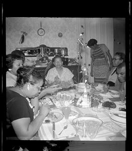 A group of people are seated eating at a dining table, including Lottie Miller and Yvonne