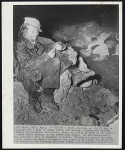 Taking a Break--Wearing an old GI cap, a raincoat and a pair of muddy boots, Pat Murphy, 23-year-old medical student at Creighton University, rests on a pile of dirt as she takes a break while working on the levee last night. In the background a man lies on a pile of sandbags to relax. Volunteers manned the weak points along the dikes throughout the night in an effort to stave off the waters of the flooding Missouri river.