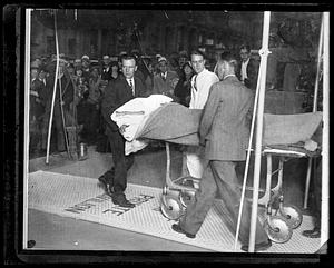 Three men wheel a covered body out on a gurney