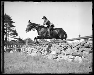 Horse and rider jumping over a low stone wall