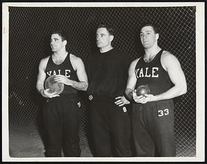 Yale's "Hardware Twins," Vic Frank, left, and Jim Fuchs, right, seen above with Frank Ryan, assistant Eli coach and weight mentor, are rated as sure point producers in the Heptagonal Games, and Fuchs will be gunning for a new indoor record in the shot put. When the spring rolls around, these two include the discus in their repertoire and reverse their positions with Vic winning and Jim trailing close behind. Vic, captain of the Yale team, is the intercollegiate discus champ.
