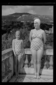 Young woman and girl standing outside in bathing suits and caps