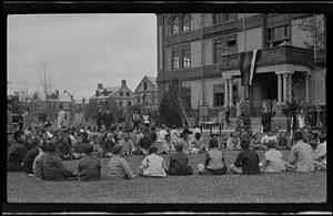 Circle of mostly children seated outside a College building