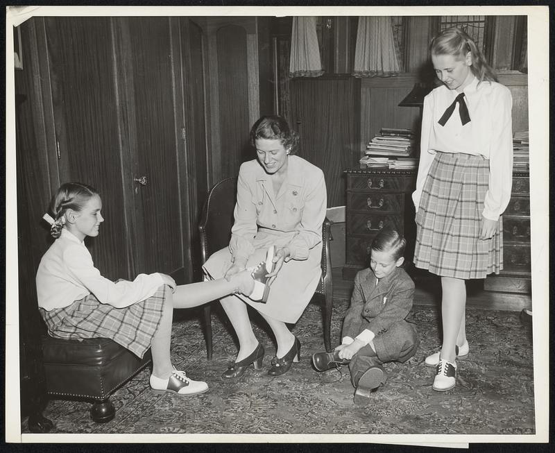 The Governor's children get new Spring shoes. Celebrating New England Shoe Market Week (April 7-11) the New England Shoe and Leather Association presented Carol Ann (left) age 11, Maurice, Jr., seated by his Mother; and Helen Tobin, age 12, each with two new pairs of shoes. Mrs. Tobin tries them on the children for size. The shoes - products of New England's second largest industry - were made to order for the Tobin children by Samuel Slosberg, a Boston manufacturer serving on the New England Shoe Market Week committee. Approximately 3000 shoe buyers, salesmen, and manufacturers will come to Boston from all parts of the United States, Canada, and Latin America during Shoe Market Week to view the styles being shown at the Statler, Copley-Plaza, and Touraine Hotels and in slaesrooms of the Boston shoe district.