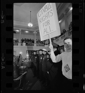 Man on ground floor of Boston Redevelopment Authority hearing holding up sign "Civil Rights for all"