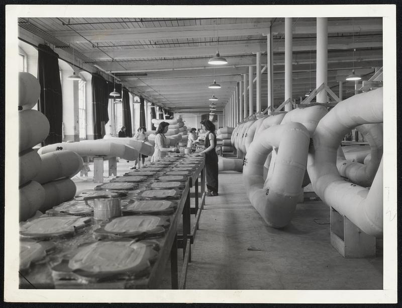 Life Rafts in Process at a New England plant, where hundreds go through the assembly line each day. Rigid inspection of each part of the assembly is a 'must.' This view shows part of the seat installation process for the rafts.