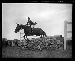 Horse and rider jumping over a low stone wall