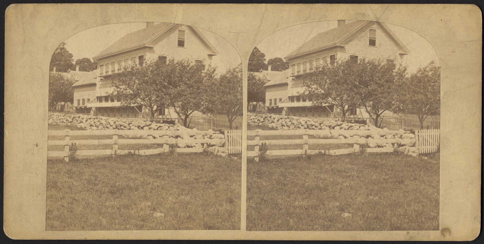 Field bound by rock and wooden fences, with building beyond