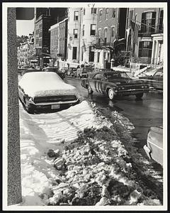 Traffic Snarlers are snow-bound cars still left on Boston streets. This is Beacon street, where abandoned car interrupted plowing for two more car lengths.