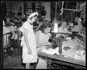 A girl watching a woman use a sewing machine in a group