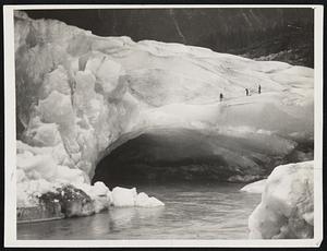 A Glacier Cavern. White ice changing through all shades of blue to purple black in the innermost recesses allows a river formed in the heart of the mighty glacier to make its exit from a majestic cavern. One of Fr. Hubbard’s photographic shots.