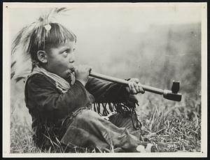 He Learns to Smoke in the Open. The Indian boys on the Glacier National Park Reservation don't have to hide behind the barn to get their smokes. The Pipe of Peace is an "honorable institution" and the young ones are supposed to learn how to puff with poise. The first smoke does not make them sick, however as they use kinnikinick instead of tobacco. Here you see one of the younger tribesmen hitting the pipe.