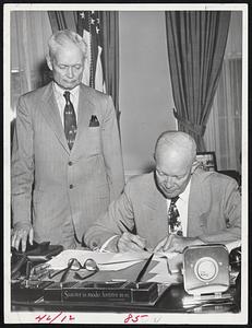 Palace Guard? Presidential Assistant Sherman Adams stands by as President Eisenhower signs a bill at his White House desk. Republican Sen. Styles Bridges has charged that Eisenhower is surrounded by a palace guard that is not keeping him fully informed. If so, Adams is the logical candidate for chief guard.