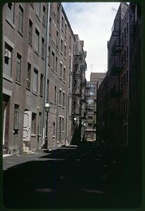 Looking down an alley, fire escapes hanging from buildings
