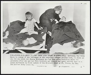 Red Cross Aids Infant Evacuees:- Edna Davidson, Red Cross Nurse in charge of the infirmary at the temporary refugee shelter here, is shown as she fed six month old Sharon Hutcheson who had been given Penicillin shots for pneumonia after she and her five brothers and sisters had spent several days in a house surrounded by flood waters of the Missouri river at Ft. Pierre, S. Dak. Her brother Bobby looks on.