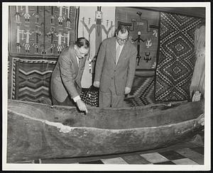 Rudolph F. Haffenreffer III, left, and Dr. Barnaby C. Keeney examine an Indian dugout found in the Penobscot Bay area in Maine. Behind them is a panel of colorful Indian woven rugs.