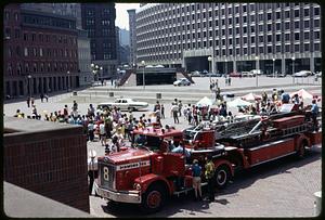 A crowd of people on Boston City Hall plaza, fire truck in foreground, police car in background