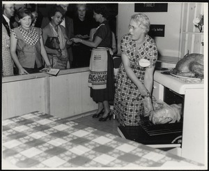 Eastern States Exposition. Mass. State Building. Mrs. Joseph Davis, demonstrating the proper way to roast a turkey while Mrs. Donald Sistare (Paxton, Mass.) passes out folders. This is at the Mass. Turkey Growers display.