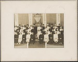 Male and female students in caps and gowns seated on risers backed by banners reading "Press, Religion, Assembly, Speech" and a sign above reading "Youth Marches On"