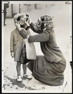 British Mother Drills Son for Gas Masks Attack. Great Britain, to prepare civilians for war, now is staging a “war” in the south of England. This British mother hears the warning of an “air raid” and “gas attack” while out shopping. Quickly she dons a gas mask and fits another over little son’s head.