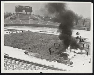 Thawing Out Wrigley Field For Championship Football Game. To insure proper playing conditions for the National Professional Football championship game between the Chicago Bears and the Washington Redskins this coming Sunday, workmen are sprayung gasoline on the field and then setting it a fire to melt the surface ice and soften the frozen playing sod to a depth of 6 inches. Hot blasts from an asphalt heater are also being used. Following this procedure a layre of straw and a tarpaulin was spread over the whole field.