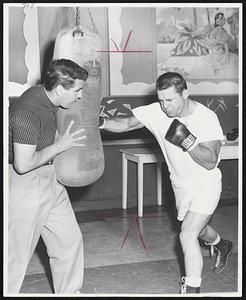 Billy Ryan of Lowell grimaces as he throws a right-handed punch at the bag held by trainer Allie Colombo, Ryan, termed a carbon copy of Rocky Marciano, meets Milton Ebbs at Mechanics Building tomorrow night in a 10-rounder.