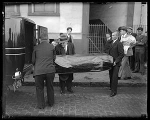 A covered body in a being put into the back of a car