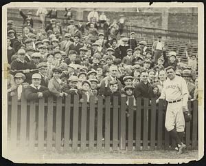 Babe Ruth poses with a crowd, a fence between them