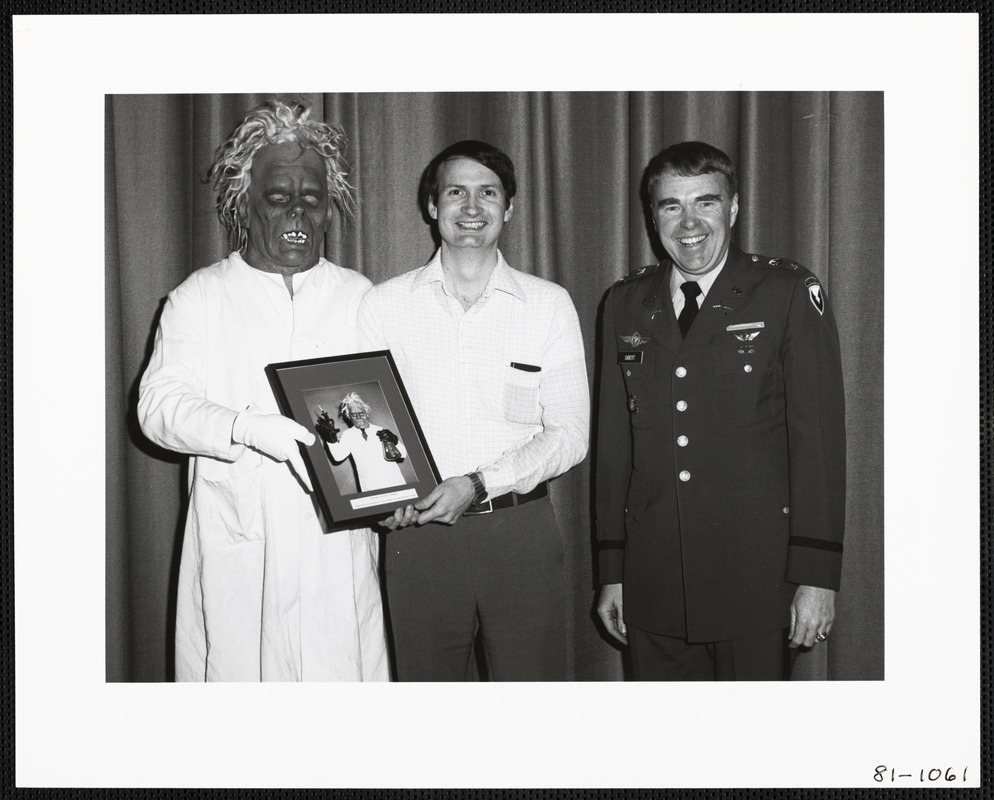 Men presenting photograph to man in mask