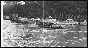 Splashing Along Charles Street between Boston Common and the Public Garden, these cars found the water hubcap-deep and the going mighty slow. Cosimo DeChiara of Waltham, whose car engine stalled in the water, rolled up his trousers and waded out of the flooded Charles street area. He was on his way to a wedding. Scenes like these were common throughout Greater Boston yesterday as cloudbursts dumped up to three inches of rain on the area. But art lovers flocked to the Public Garden.