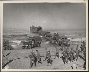 A tank lighter unloads trucks on the beach near Gela, Sicily, as American soldiers stand by