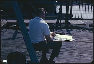 Back view of artist sitting and working on pier