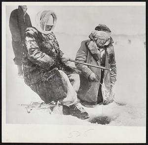 Fisherwomen, Winter Style - A real fisherman won't forsake the sport just because 10-below weather is made worse by 40-mile winds. Participants in contest on Lake Minnetonka at Wayzata, Minn., are Mrs. Frances Johnson, 62-year-old grandmother, holding ice fishing rod, and her sister, Mrs. Marie Long, 58, ladling ice from the hole. Both live in St. Paul.