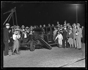 People stand by a wrecked car about to be towed away