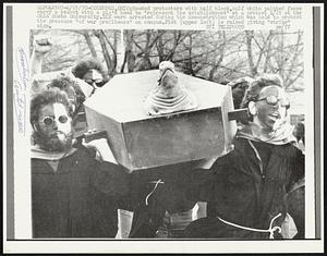 Hooded protesters with half black, half white painted faces carry a casket with a pig's head to "represent the establishment" at a protest 4/21 at the Ohio State University. Six were arrested during the demonstration which was held to protest the presence "of war profiteers" on campus. Fist (upper left) is raised giving "strike" sign.