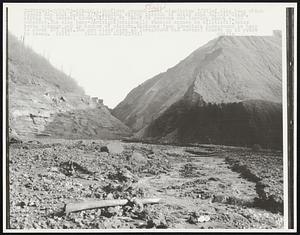 Lorado, W. VA: First ground level view (taken 2/28) of slag heap which formed dam that burst 2/26, sending raging torrent of water down Buffalo Creek, wiping out several towns, killing at least 66 persons and leaving about 4,000 homeless. The slag heap-dam (right) originally reached across to hill (left). Water broke through gap in center of picture. Distance from immediate foreground to heap is about 300 feet. The now clear are in foreground had several houses on it prior to break.