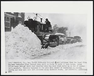 Johnston, Pa. - Big Blow - Air National Guard bulldozer from the local 876th Engineer Battalion plows through deep drift on Route 53 north of here today. Autos follow dozer through drift that resulted when big wind storm moved in on top of yesterday's snowfall. Numerous highways in the area were closed or restricted to one-way traffic and many cars were left stranded along district roads.