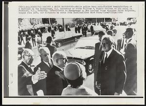 Arrival Against a Noisy Background -- While police keep anti-Vietnam demonstrators at a distance in the background, U.S. Secretary of State William P. Rogers arrives at his hotel in Auckland, N.Z., Saturday. Identifiable in foreground is New Zealand Prime Minister Keith Holyoake, second from left.
