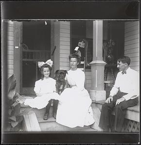 Girl, woman and man, with dog, on stoop of house