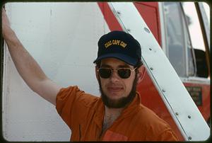 Man wearing CGAS Cape Cod hat standing next to helicopter