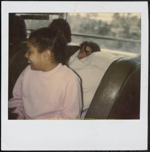 Girl in pink smiling next to sleeping friend on bus