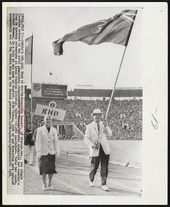 Canada’s One-Girl Team In Moscow – Ernestine Russell, of Windsor, Ont., the single Canadian entrant in the world gymnastics championships at Moscow, parades alongside her country’s flag in opening ceremonies at Lenin Stadium Saturday, before 100,000 spectators. Today her coach, Bernard Newman, in a call to his home at Windsor, from Vienna, said he and Ernestine were ushered prematurely out of the Soviet Union by the Moscow government.