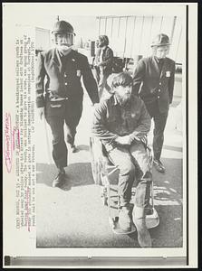 Arrested in Antiwar Protest- A handicapped college youth is wheeled away by the police after his arrest for blocking buses loaded with draftees at Boston Army Base today. The youth, who declined to give his name, was among group of over 300 students masses at gate in antiwar demonstration organized at Harvard. The youth said he was not a war veteran.