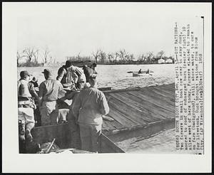 Get Rations--Two farmers in small boat row over to Army duck, moored to roof of submerged barn (center right) 10 miles west of here today. Farmers elected to remain on farm (background), still above water, to care for livestock. Duck brought rations from Sioux City.