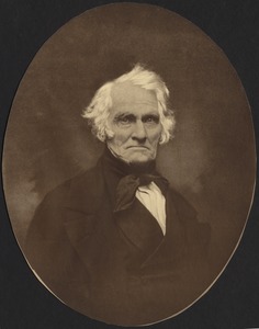 Early photo of older man in with white hair, wearing dark suit with high collar