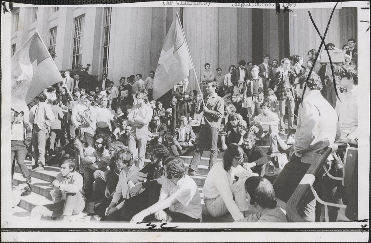 Students of Massachusetts Institute of Technology and Harvard University are among demonstrators who assembled on the steps of the main entrance to MIT in Cambridge, Mass., Friday displaying two flags identified as National Liberation Front (Viet Cong) flags of North Vietnam