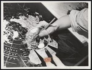 The Map Maker in a Changing World. A cartographer assisted by a magnifying glass, correcting the new boundary of Czechoslovakia on a negative key plate of middle Europe. These corrections or changes are made before the new map strips are printed. Following the printing, these strips are mounted onto globes which are the fitted onto stands.